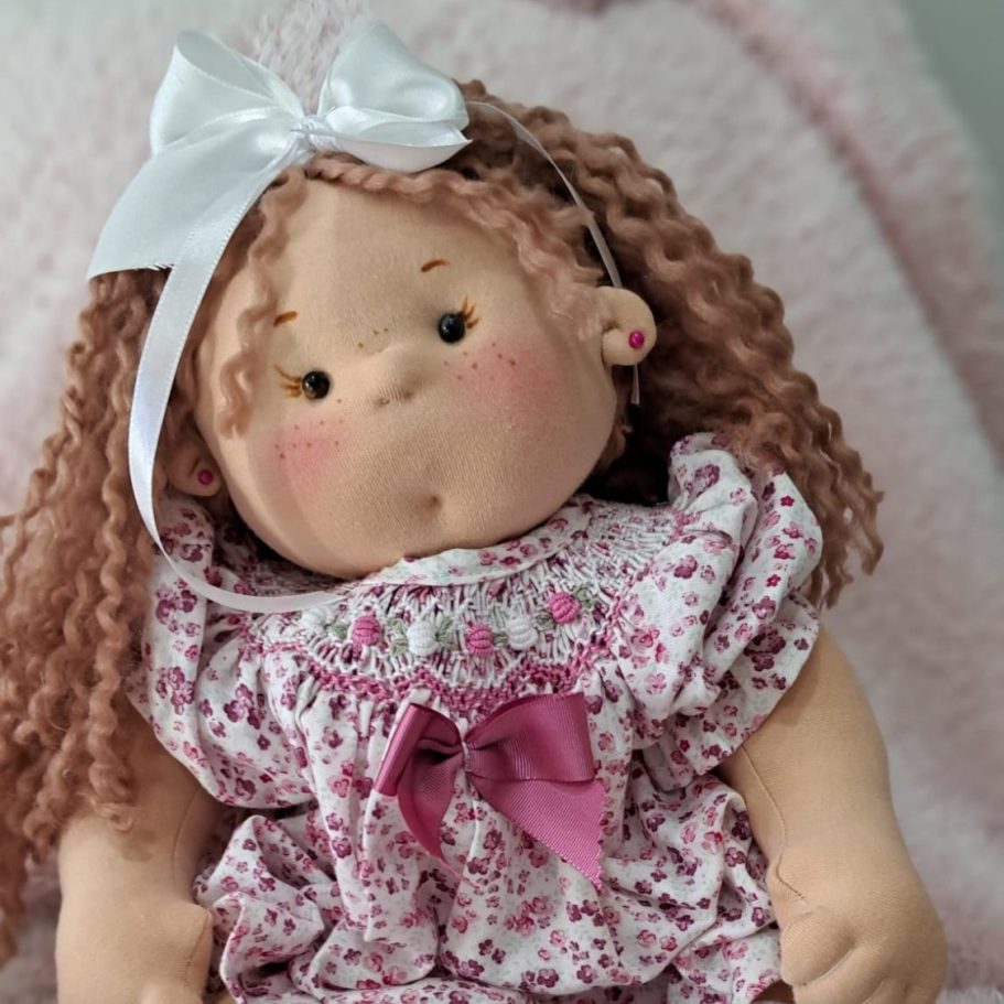 muñeca personalizada regalo unico baby doll Muñeca de tela con pelo rizado, vestida con un vestido floral y un lazo rosa.
