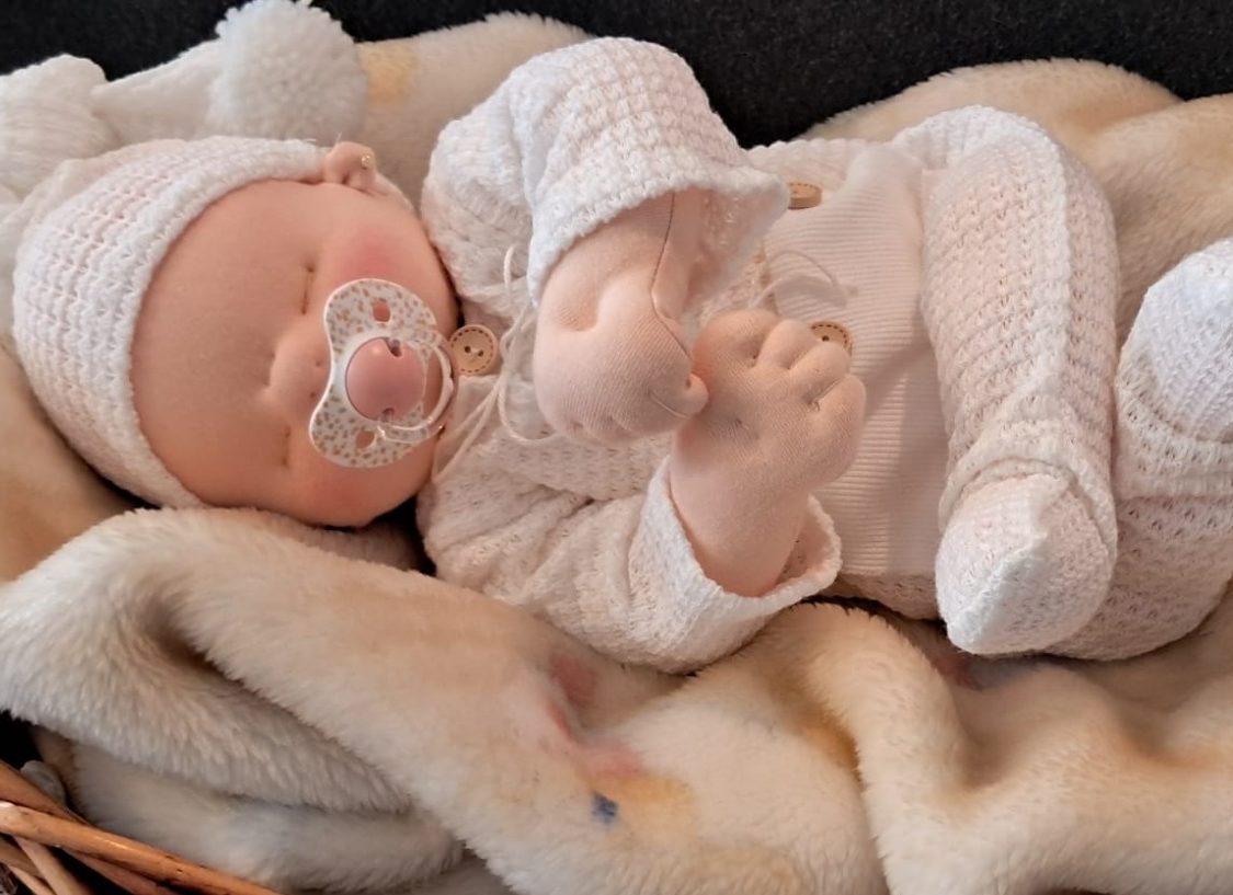 muñeca bebé personalizado unico regalo baby doll Bebé de juguete con chupete, vestido de blanco, acostado en una manta suave.